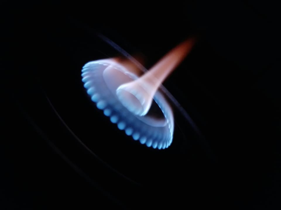 A ring of blue gas flame on a burner against a dark background