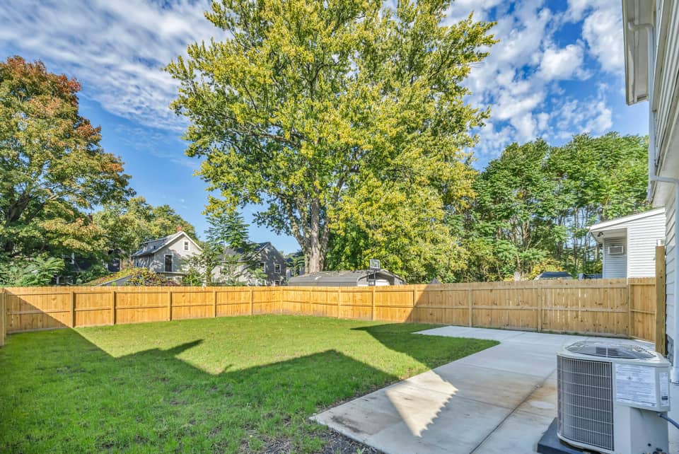 An outdoor air conditioning condenser on a concrete pad at the edge of a fenced backyard lawn