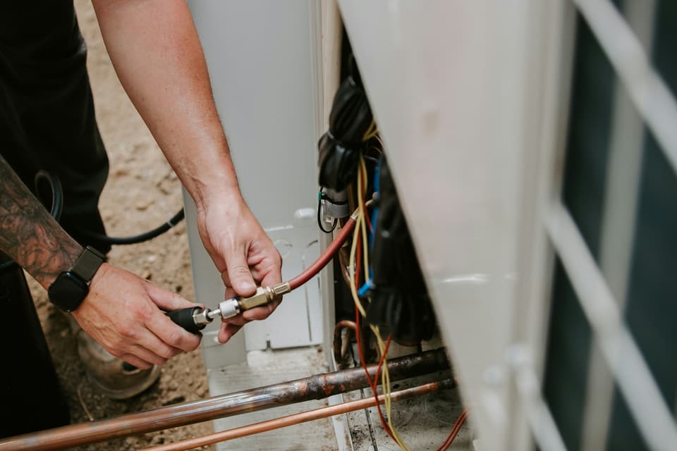 Hands connecting a gauge hose to the service valve of an outdoor air conditioning unit