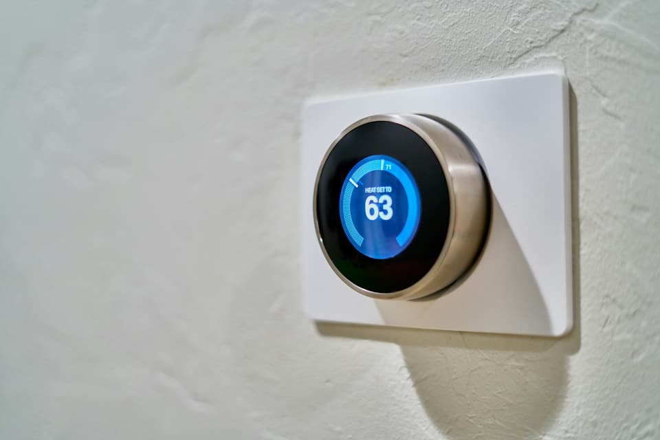 A round smart thermostat on a wall, its display set to heat to 63 degrees